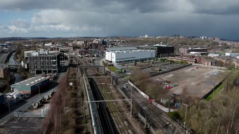 Aerial-footage-of-trains-approaching-Stoke-on-Trent-train-station-in-the-midlands-by-the-canal,-waterside-and-A50-motorway