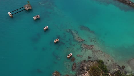 Aerial-view-of-old-bridge-mounts-in-clear-turquoise-water-by-tropical-island