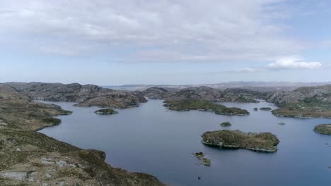 Sideways-aerial-of-a-wide-lake-full-of-small-islands-in-a-rocky-and-moorland-setting,-Northern-Europe