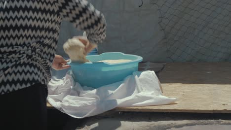 Eine-Afghanische-Frau-Nimmt-Teig-Aus-Dem-Becken,-Um-Ihn-Zum-Brotbacken-In-Einem-Selbstgebauten-Tandoor-Im-Flüchtlingslager-Vorzubereiten
