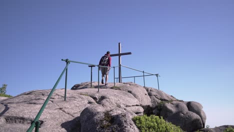Young-tourist-man-climbed-on-top-of-a-hill-with-beautiful-wooden-cross