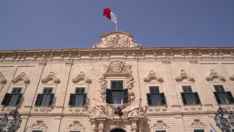 Auberge-De-Castilla-In-Valletta,-Malta-Push-Out-Gimbal-Dolly-Aufnahme-Mit-Wehender-Flagge-Und-Fliegenden-Vögeln