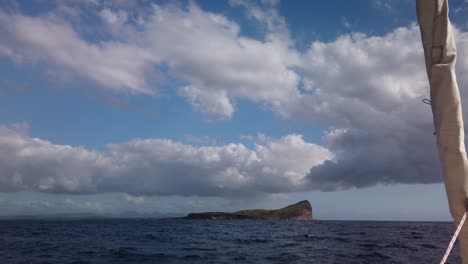 Eine-Aufnahme-Vom-Bug-Eines-Katamarans-Auf-Einer-Kleinen-Insel-Mit-Einer-Klippe-Auf-Der-Rechten-Seite,-Unter-Riesigen-Wolken