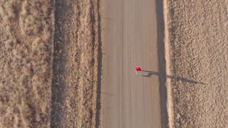 Birds-eye-view-of-runner-running-on-a-gravel-road-during-winter-morning