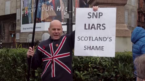 A-slow-motion-and-close-up-of-a-British-Unionist-holding-up-a-sign,-'SNP-LIARS,-SCOTLAND'S-SHAME'