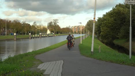 Young-family-cycling-on-path-beside-canal,-Netherlands,-still-shot