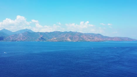 The-Peaceful-Movement-Of-The-Water-Background-WIth-High-Mountains-And-Bright-Cloudy-Sky-During-Summer,-Indonesia-Deep-Blue-Ocean---Wide-Shot