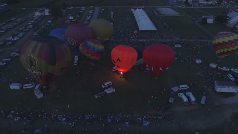 Luftaufnahme-Von-Heißluftballons,-Die-Sich-Für-Eine-Nächtliche-Flammenshow-Bei-Einem-Ballonfestival-Bei-Sonnenuntergang-Füllen,-Wie-Von-Einer-Drohne-Gesehen