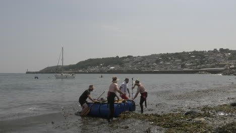 Local-business-team-finishing-at-the-Newlyn-raft-race-charity-fun-outdoors-event,-Cornwall