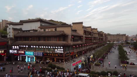Xian,-China---July-2019-:-Crowds-walking-on-streets-and-town-square-with-landmark-Bell-Tower-in-the-background,-as-seen-from-the-viewing-terrace-in-the-Drum-Tower,-Shaaxi-Province