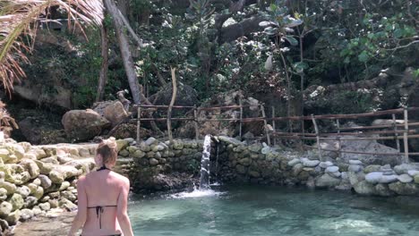 Woman-in-bikini-and-with-blond-hair-bathing-in-a-natural-pool-with-a-little-waterfall-in-Bali,-Indonesia