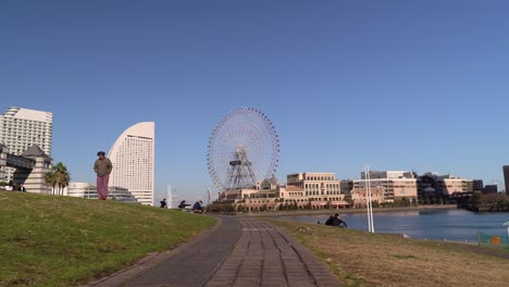 Gente-Disfrutando-Del-Clima-En-Yokohama-Japón-Con-Rueda-De-Ferris-Y-Un-Edificio-Alto-En-El-Fondo---Plano-General