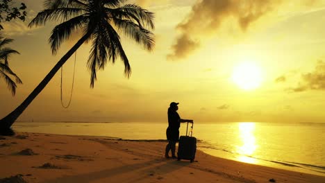 Wunderschöner-Goldener-Sonnenuntergang-über-Dem-Sandstrand-Mit-Palmen-Und-Einer-Frau,-Die-Das-Gepäck-Hält