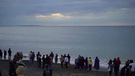 Strand-In-Japan-–-Menschen-Warten-Am-Ufer-Auf-Den-Sonnenaufgang,-Während-Die-Wellen-An-Einem-Kalten-Morgen-Plätschern-–-Weitwinkelaufnahme