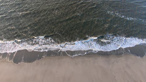 Aerial,-static,-drone-shot-of-calm-waves-hitting-a-beach,-on-Langeoog-island,-on-a-sunny-day,-in-North-Germany