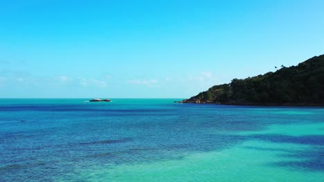 Blue-azure-sea-water-washing-beautiful-rocky-coastline-of-tropical-island-at-sunrise-with-bright-sky