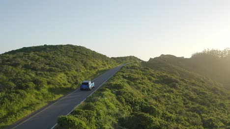 Blue-Porsche-Macan-driving-through-theMarin-Headlands-in-San-Fransisco,-California,-at-golden-hour,-Aerial-follow-shot