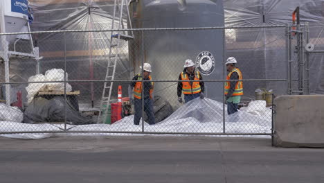 Trabajadores-De-La-Construcción-Trabajando-Juntos-Para-Colocar-Una-Lona-De-Plástico-En-El-Centro-De-Denver,-Colorado