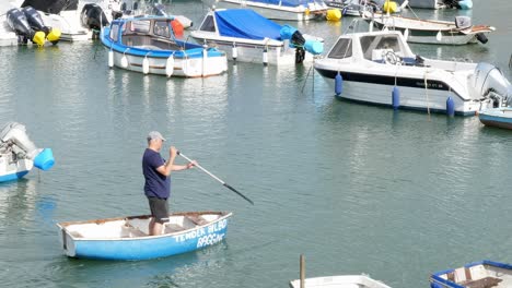 Ein-Mann-Rudert-Lässig-Im-Stehen-In-Einem-Kleinen-Boot-In-Einem-Belebten-Hafen