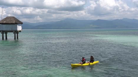 Touristen-Kajakfahren-Auf-Dem-Tropischen-Blauen-Ozean-In-Der-Nähe-Der-Cottages-Im-Dos-Palmas-Island-Resort-Und-Spa-In-Honda-Bay,-Puerto-Princesa,-Palawan,-Philippinen