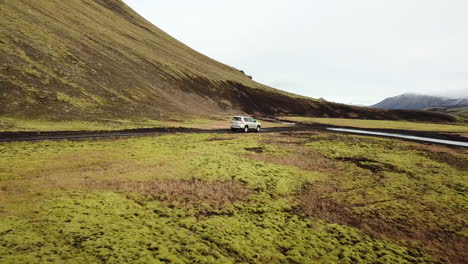 Four-Wheel-Crossover-SUV-on-Urban-Expedition-in-Iceland-Rural-Landscape-Crossing-Over-Shallow-River,-Tracking-Aerial
