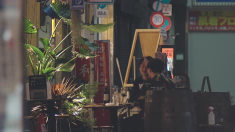 Two-Japanese-Friends-Chatting-Happily-At-The-Outdoor-Seating-Of-A-Restaurant-At-Night-In-Kamata,-Tokyo,-Japan