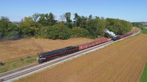 Luftaufnahme-Einer-Antiken-Dampflokomotive,-Die-An-Einem-Sonnigen-Herbsttag-Mit-Güterwaggons-Durch-Amisches-Ackerland-Am-Bahnhof-Angehalten-Hat,-Gesehen-Von-Einer-Drohne