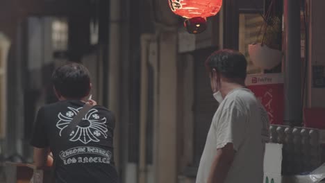 Zwei-Japaner-Rauchen-Nachts-Mit-Abgenommenen-Masken-Vor-Dem-Japanischen-Restaurant-In-Kamata-In-Tokio,-Japan,-Während-Der-Coronavirus-Pandemie
