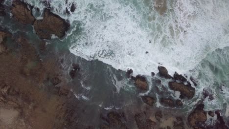 Waves-breaking-on-shore-rocks-with-flying-birds,-high-vertical-aerial