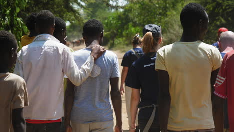 Local-people-and-charity-event-staff-walking-in-small-unpaved-road-located-in-Ziway-outside-Addis-Ababa,-Ethiopia