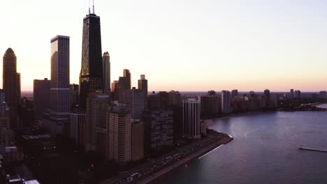 Aerial,-Chicago-John-Hancock-Center-overlooks-Lake-Michigan-and-busy-road-at-sunset