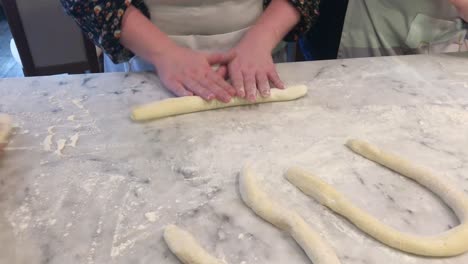 Detail-shot-of-group-of-various-people-rolling-out-pasta-dough-by-hand-on-a-marble-countertop