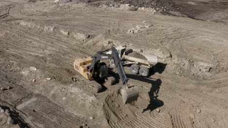 Aerial-circling-shot-of-a-John-Deere-450D-excavator-loading-dirt-into-a-rock-truck-on-a-construction-site