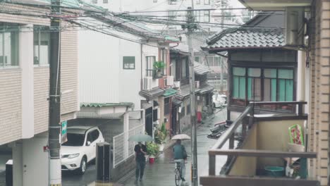 Gente-Caminando-Y-Andando-En-Bicicleta-Con-Paraguas-En-La-Calle-Japonesa-En-Un-Día-Lluvioso-En-Kyoto,-Japón