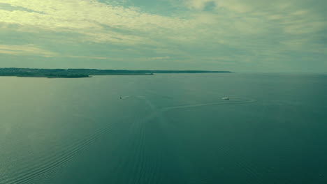 Two-motorboats-on-clear-and-calm-sea,-aerial-shot-slow-motion-wide-horizont