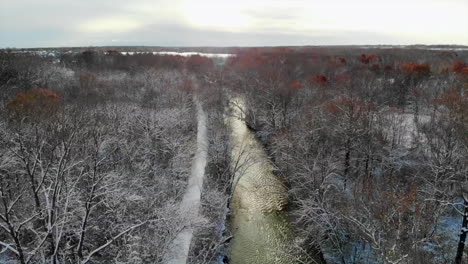Vista-Panorámica-Aérea-Del-Arroyo-Que-Corre-Durante-El-Amanecer-En-Un-Bosque-Cubierto-De-Nieve-En-Michigan