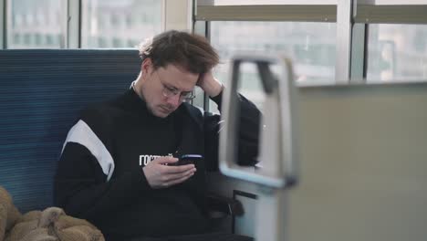 Caucasian-Man-Sitting-And-Looking-At-His-Smart-Phone-On-A-Moving-Train-In-Tokyo,-Japan