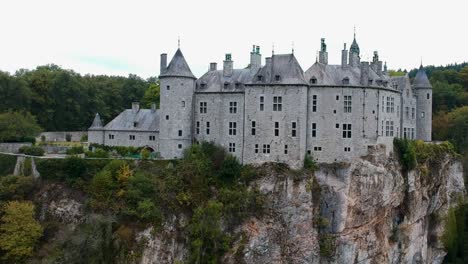 Aerial-shot-of-imposing-castle-on-a-rocky-cliff-surrounded-by-wood