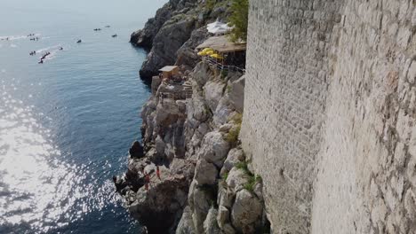 Panning-up-view-of-Dubrovnik's-city-wall-from-the-south-side-with-tourists-in-kayaks-beyond-during-covid-times