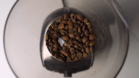 Up-close-overhead-view-of-fresh,-brown-coffee-beans-being-poured-into-fancy-electric-grinder-for-morning-coffee