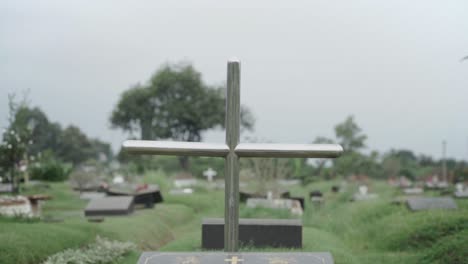 Metal-cross-over-grave-with-memorial-plaque-at-lawn-cemetery,-close-up