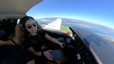 Young-female-pilot-with-sunglasses-flying-a-small-private-plane,-looking-around-and-smiling