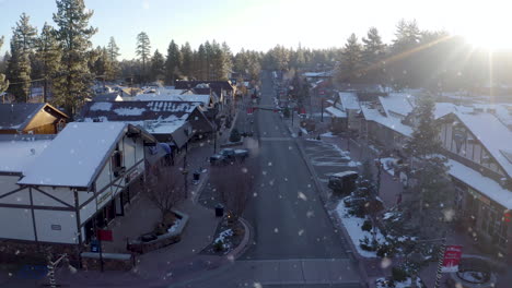 Early-Morning-Drone-aerial-between-Big-Bear-Lake-street,-CA-with-winter-snowfall---sunshine-flares