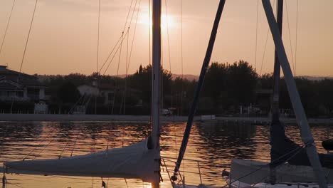 Segelbootmasten-Im-Gegenlicht-Der-Untergehenden-Sonne,-Goldener-Sonnenuntergang-Am-Gardasee,-Italien