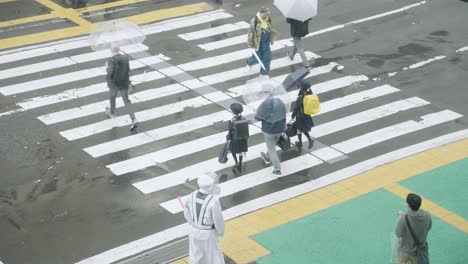 Japanische-Grundschulkinder-überqueren-Mit-Ihren-Eltern-An-Einem-Regnerischen-Tag-Die-Straße-In-Shibuya-–-Hoher-Winkel,-Zeitlupe