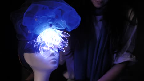 A-student-working-on-a-weird-futuristic-manikin-head-with-fluorescent-color-changing-led-light-flower-design-hat-for-a-design-project