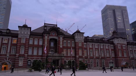 Fast-pan-across-Tokyo-station-at-dusk-with-skyscrapers-in-background-and-commuters-walking