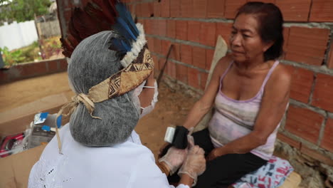 Amazonian-tribal-healer-volunteering-as-a-COVID-19-nurse,-speaking-with-a-patient-in-her-tribe