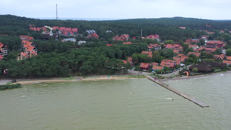 Luftaufnahme:-Rotierende-Aufnahme-Einer-Bucht-Voller-Kitesurfer-Und-Häuser-Im-Hintergrund