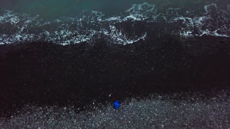 Luftaufnahme-Von-Oben-Nach-Unten:-Junge-Wirft-Vulkanische-Kieselsteine-Ins-Meer